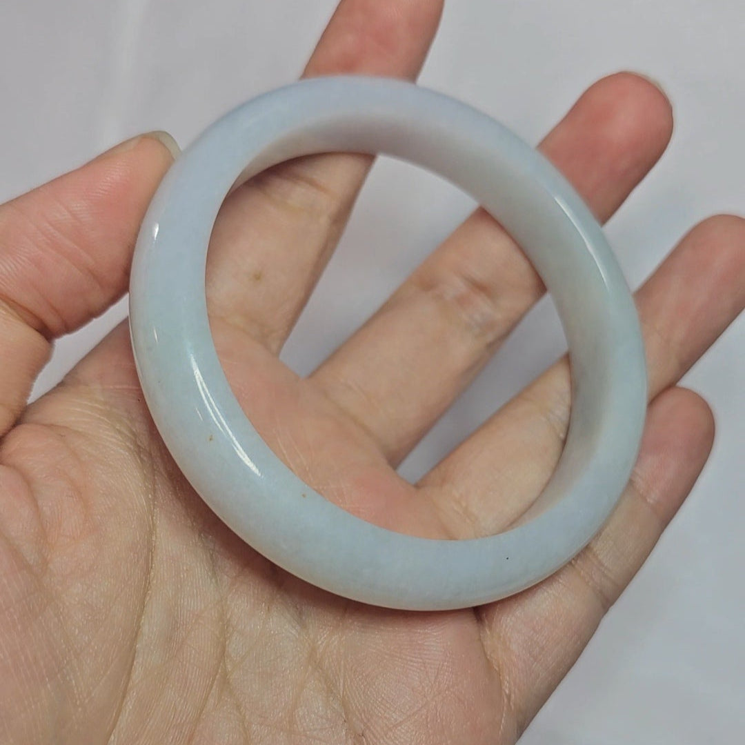 Hand holding a round, light-colored stone against a plain background