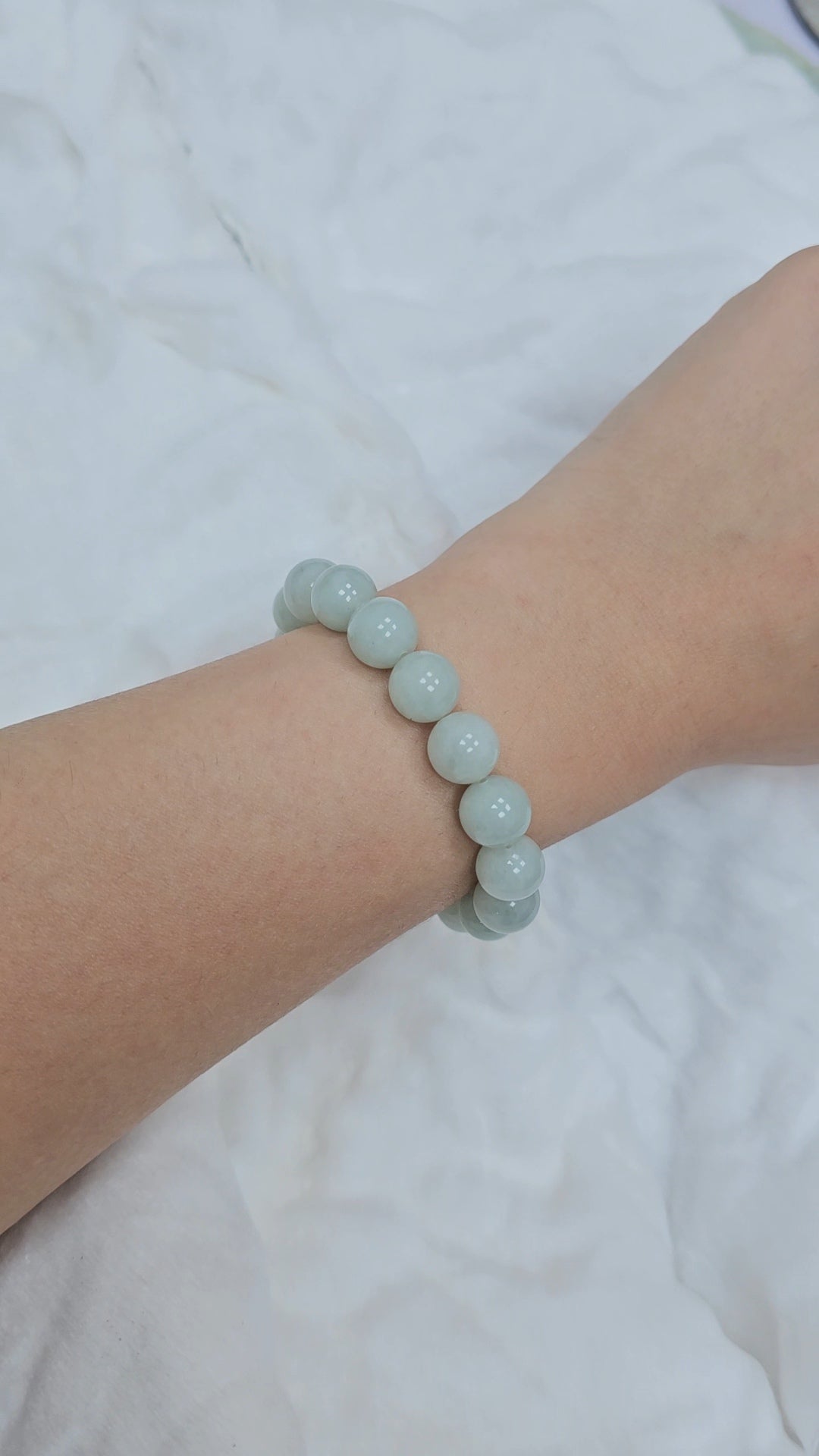 Light blue and pastel green jadeite beaded bracelet on a wrist against a white background